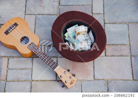 ukulele and hat with banknotes on paving slabs. 106662191