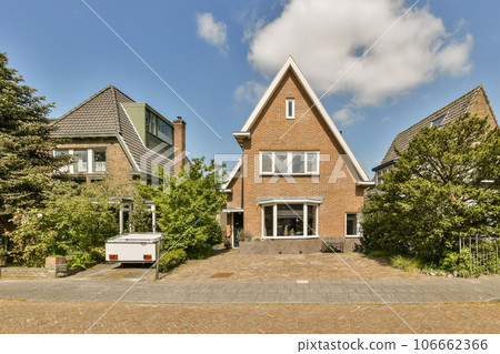 a brick house in the middle of an area with trees and bushes on either side, there is a blue sky 106662366