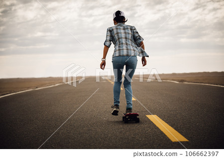 Asian woman skateboarder skateboarding on trail cross the desert Asian woman skateboarder skateboarding on trail cross the desert 106662397