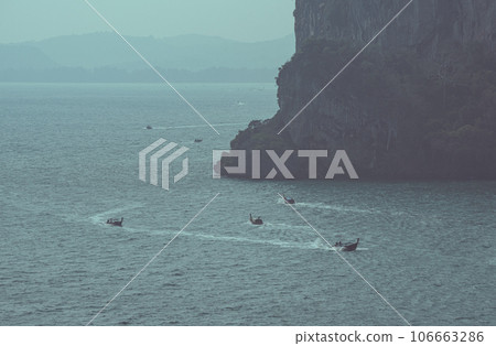 Long-tail boats go around a ledge of a limestone mountain, sailing on the evening sea. This is the route from Ao Nang Town to Railay Beach. Krabi Province, Thailand Long-tail boats go around a ledge of a limestone mountain, sailing on the evening sea. This is the route from Ao Nang Town to Railay Beach. Krabi Province, Thailand 106663286