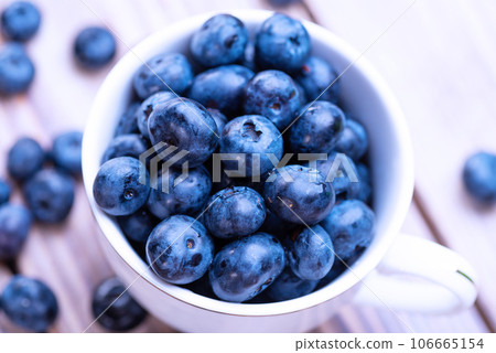 Freshly picked organic blueberries in a white cup on a light wooden table 106665154