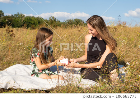 A five-year-old daughter gives a gift to her mother in nature in the summer field. Mother's Day, Happy Parenthood. A five-year-old daughter gives a gift to her mother in nature in the summer field. Mother's Day, Happy Parenthood. 106665775