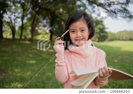 Asian girl thinking about studying in the garden. She is taking notes in a notebook. Asian girl thinking about studying in the garden. She is taking notes in a notebook. 106666203