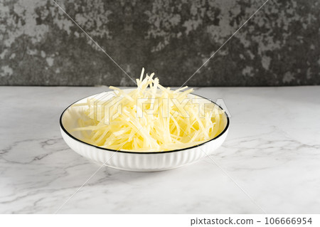 Sunlight illuminates the bowl of sliced potato shreds on a cut marble slab. 106666954