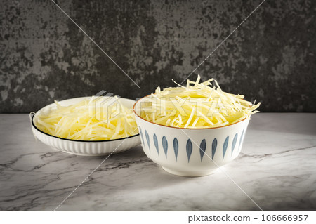 Sunlight illuminates the bowl of sliced potato shreds on a cut marble slab. 106666957