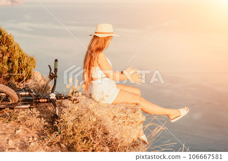 A woman cyclist on a mountain bike looking at the landscape of mountains and sea. Adventure travel on bike. A woman cyclist on a mountain bike looking at the landscape of mountains and sea. Adventure travel on bike. 106667581