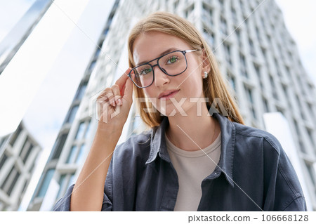 Teenage female in glasses looking at camera, glass skyscrapers background 106668128