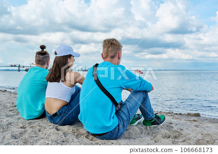 Back view of three teenage friends sitting at beach, looking at sea 106668173