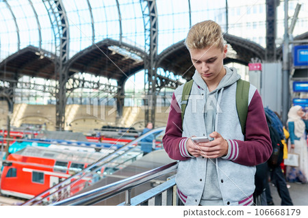 Young guy using mobile apps on smartphone standing at railway station 106668179