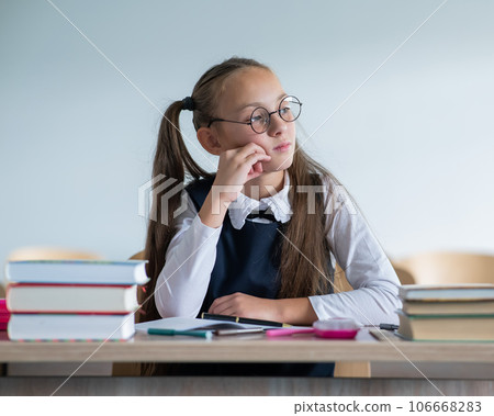 Caucasian girl with two ponytails wearing in glasses sits at a school desk. 106668283
