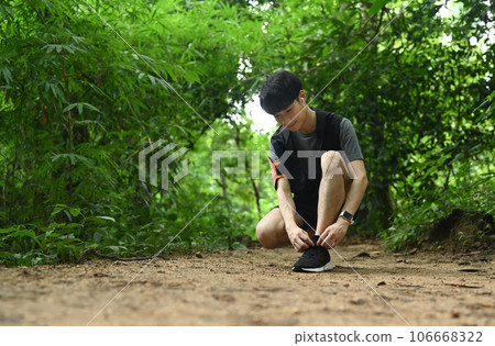 Full length of male runner tying shoes laces, getting ready for trail run in forest. Sports, adventure and healthy lifestyle 106668322