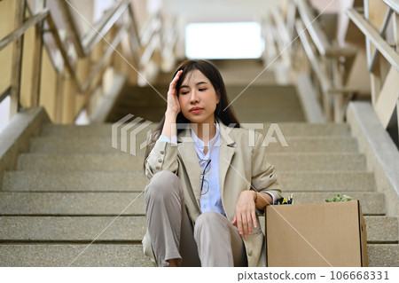Fired businesswoman sitting hopelessly sitting on stairs of a business building. unemployment, depressed and fired from job 106668331