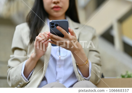 Businesswoman sitting on stairs outside office building and texting messages, chatting in social on smartphone 106668337