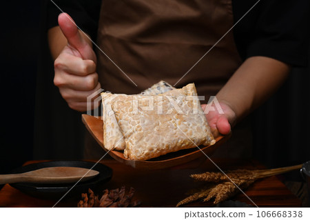 Man wearing apron holding wooden plate with homemade tempeh, healthiest alternative plant protein 106668338