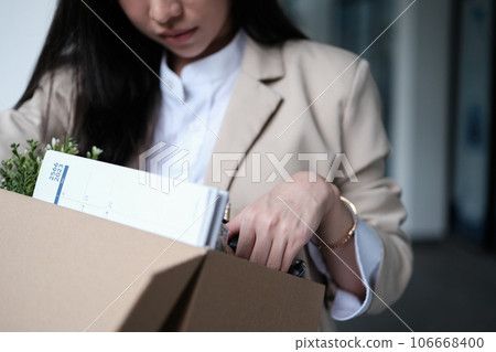 Frustrated fired female employee packing belongings in cardboard box leaving workplace. Unemployment concept Frustrated fired female employee packing belongings in cardboard box leaving workplace. Unemployment concept 106668400