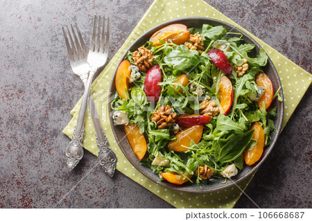 Raw salad with plums, arugula, gorgonzola cheese and walnuts close-up in a plate. horizontal top view 106668687