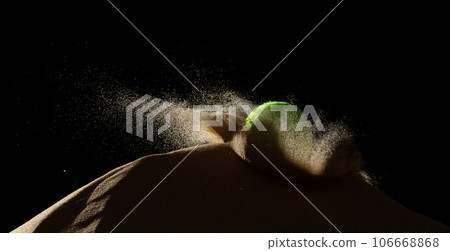 Tennis ball throw hit sand soil and Deep impact on sand hill and splash all over area. Tennis ball hit Sand dune hill over wind storm and blast dust splash over mountain. Black background isolated 106668868