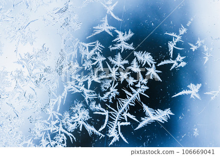 Beautiful blue white frost pattern on a window glass, macro photo Beautiful blue white frost pattern on a window glass, macro photo 106669041