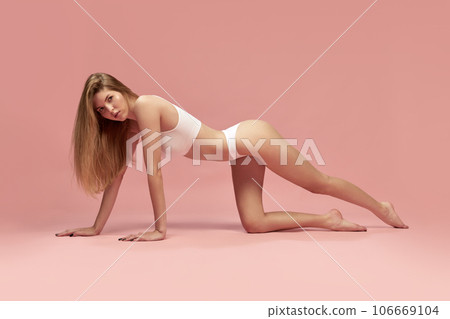 Charming young thin sportive woman in white cotton underwear posing on floor over pastel pink background. recretion, relaxing Charming young thin sportive woman in white cotton underwear posing on floor over pastel pink background. recretion, relaxing 106669104