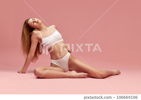 Relaxed young girl with fit, slim figure lying on floor, posing in underwear against pastel pink studio background Relaxed young girl with fit, slim figure lying on floor, posing in underwear against pastel pink studio background 106669106