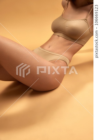 Cropped image of slim female body in beige underwear isolated over beige color background. dieting, healthy eating Cropped image of slim female body in beige underwear isolated over beige color background. dieting, healthy eating 106669123