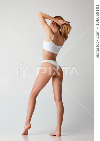 Rear view portrait of young woman with slim sporty body posing in white color lingerie over studio background. Smooth skin. Healthy back Rear view portrait of young woman with slim sporty body posing in white color lingerie over studio background. Smooth skin. Healthy back 106669181