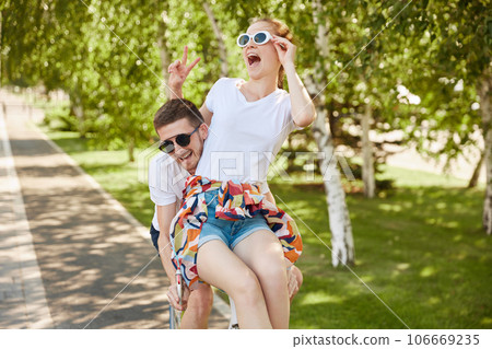 happy couple in love riding bicycle. Handsome guy and young sensual woman date. Youthful people having fun on nature, in park. 106669235