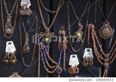 Pendants and brooches with cheap stones hang on chains. Sale of handmade jewelry at the fair. 106669633
