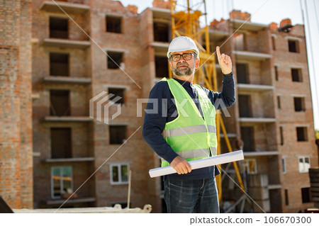 Construction site manager standing wearing safety vest. Man giving an order to workers. Construction site on a background. Construction site manager standing wearing safety vest. Man giving an order to workers. Construction site on a background. 106670300
