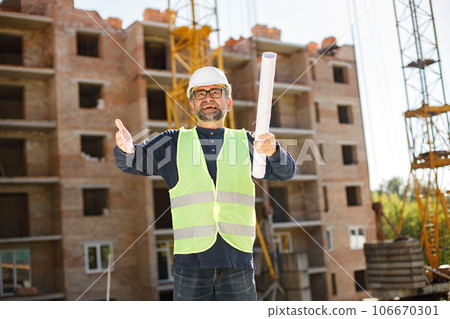Construction site manager standing wearing safety vest. Man giving an order to workers. Construction site on a background. Construction site manager standing wearing safety vest. Man giving an order to workers. Construction site on a background. 106670301