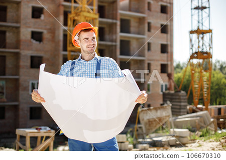 Construction site manager standing wearing helmet, thinking at construction site. Construction site on background. Man holding documents. 106670310