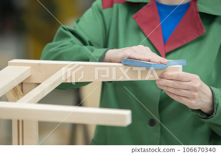 The hands of a woodworking plant worker grind wooden chairs from natural wood. The woodworking industry. The hands of a woodworking plant worker grind wooden chairs from natural wood. The woodworking industry. 106670340