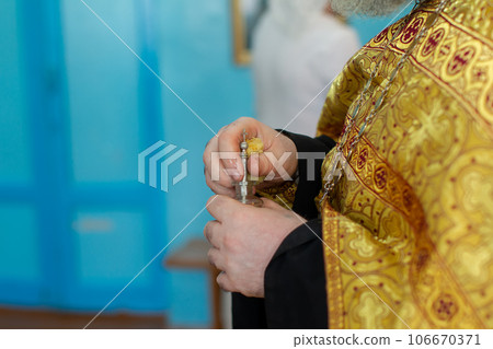 The hands of an Orthodox priest hold a bottle of myrrh oil for the rite of baptism. The hands of an Orthodox priest hold a bottle of myrrh oil for the rite of baptism. 106670371