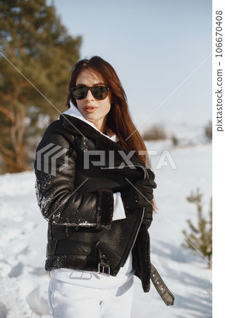 Close-up portrait of woman in black jacket. Woman standing in a forest in snowy day. 106670408