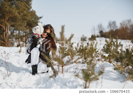 Cute girl walking in a winter park. Woman in a brown jacket. Lady with a dog. 106670435