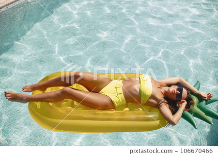Young woman floating on pineapple air mattress in pool sunbathing. Summer vacations. Young woman floating on pineapple air mattress in pool sunbathing. Summer vacations. 106670466