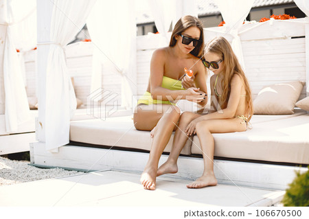 Mother and daughter going to sunbathe. Parent applying sunscreen on chils, sitting by poolside. 106670500