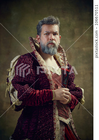 Portrait of serious nobleman, medieval king wearing female dress with fan against vintage green background 106670511