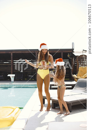 A funny woman with a child in Christmas hats by pool. Christmas celebration concept. Christmas day. Lifestyle. Pool background. 106670513