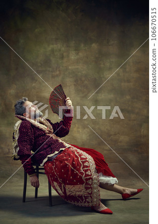 Thoughtful. Humorous representation of medieval royal person, man in female dress with fan against vintage green background 106670515