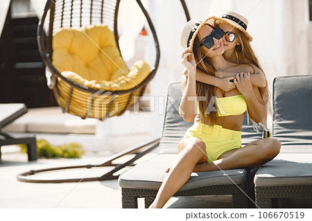 Young mother have vacation with her kid. Both wearing swimsuits sitting on soft sunbed with cocktail. Summer holidays concept, family relationship. European. 106670519