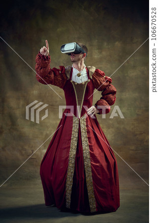 Historical education. Royal man, medieval prince in female dress wearing vr glasses against vintage green background 106670528