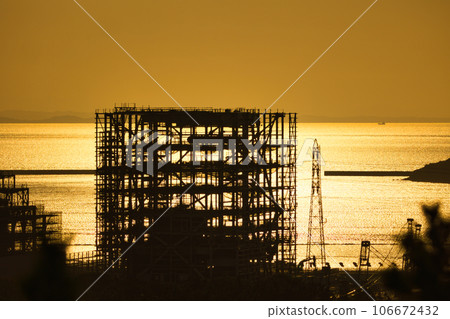 The sea shining in the setting sun and the framework of the building under construction 106672432