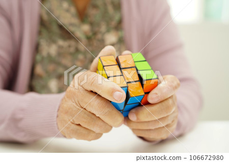 Bangkok, Thailand - May 15, 2022 Asian elderly woman playing Rubik cube game to practice brain training for help dementia prevention and Alzheimer disease. 106672980