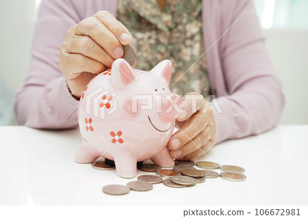 Retired elderly woman putting coins money in piggy bank and worry about monthly expenses and treatment fee payment. 106672981