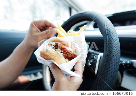 Asian woman driver hold and eat hamburger in car, dangerous and risk an accident. Asian woman driver hold and eat hamburger in car, dangerous and risk an accident. 106673016