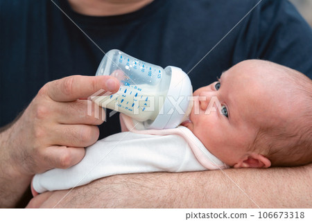 Dedicated man, as a father, bonds by feeding his newborn baby with formula bottle 106673318
