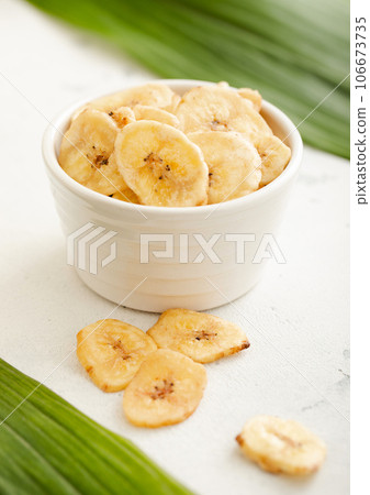 Yellow dried banana chips snack in glass bowl plate on light board. Yellow dried banana chips snack in glass bowl plate on light board. 106673735