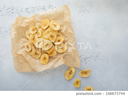 Crunchy dried banana chips on baking paper on light background. Crunchy dried banana chips on baking paper on light background. 106673744