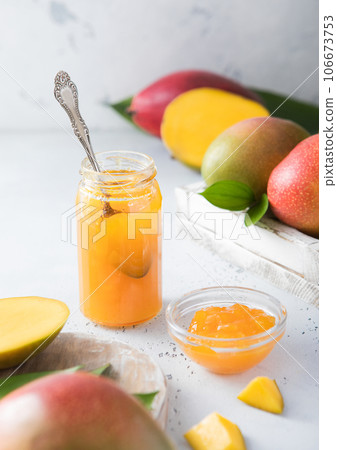 Mango marmalade jam puree with spoon on light background with raw fruits. 106673753